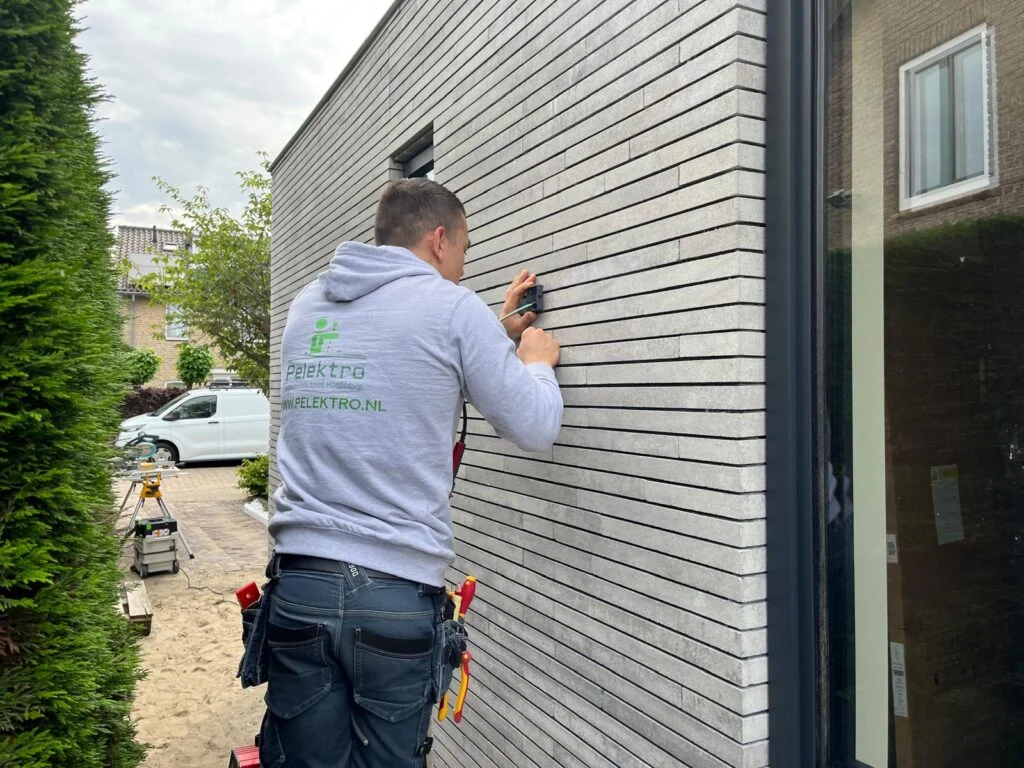 Monteur aan het werk aan een buitenwand; beeld uit de huidige website van Pelektro